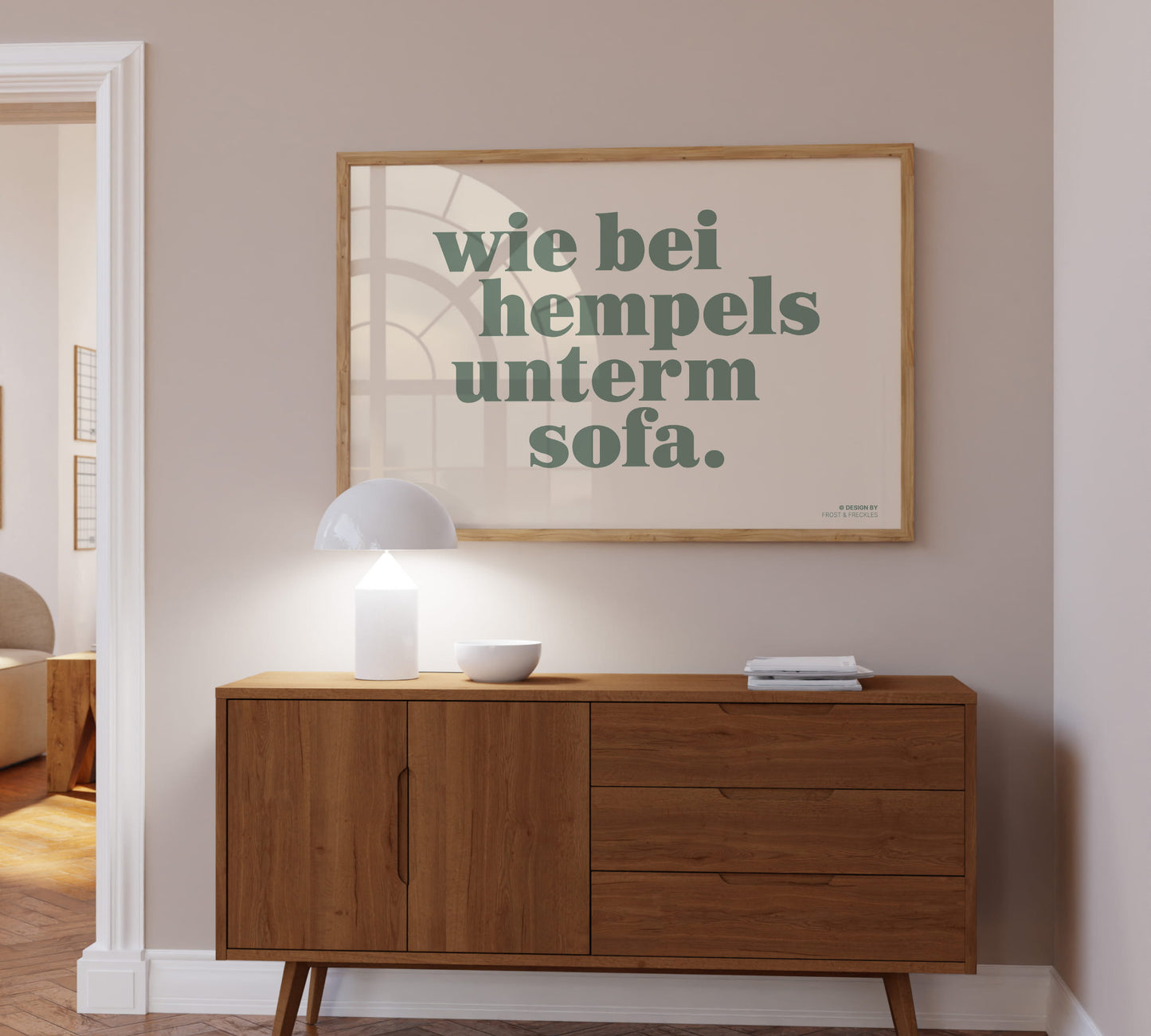 Gerahmtes Wandbild mit dem lustigen Spruch "Wie bei Hempels unterm Sofa" in einem hellen Holzrahmen über einer modernen Wohnzimmer Kommode.