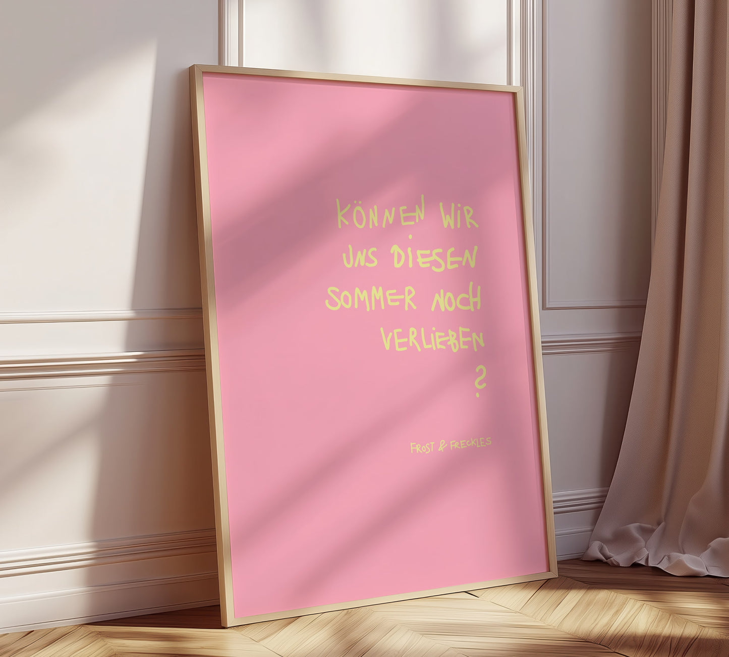 Handgeschriebenes Poster mit dem Text 'Können wir uns diesen Sommer noch verlieben' lehnt gerahmt an moderner Wohnzimmerwand