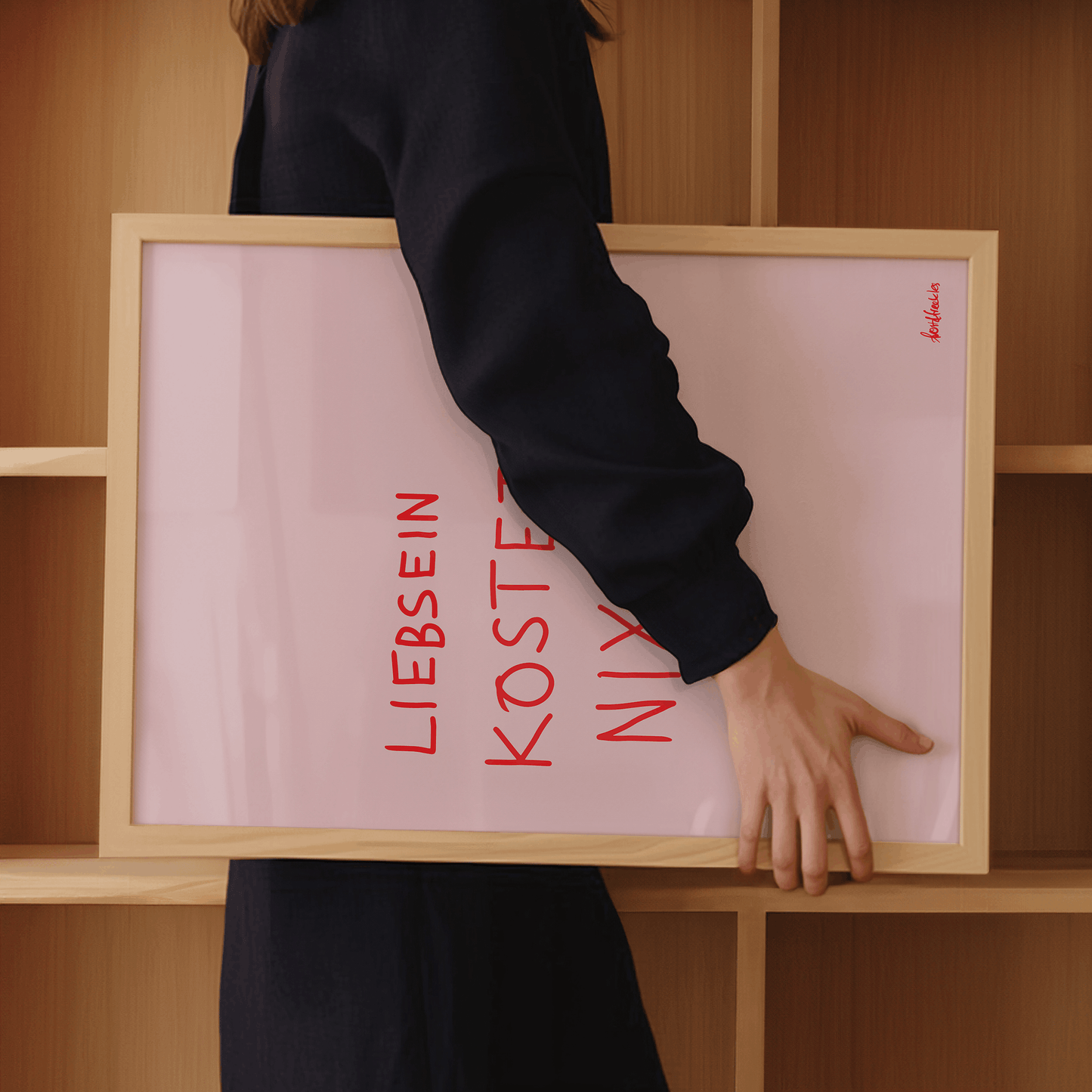Frau trägt gerahmtes Küchenposter mit Schriftzug Liebsein Kostet Nix