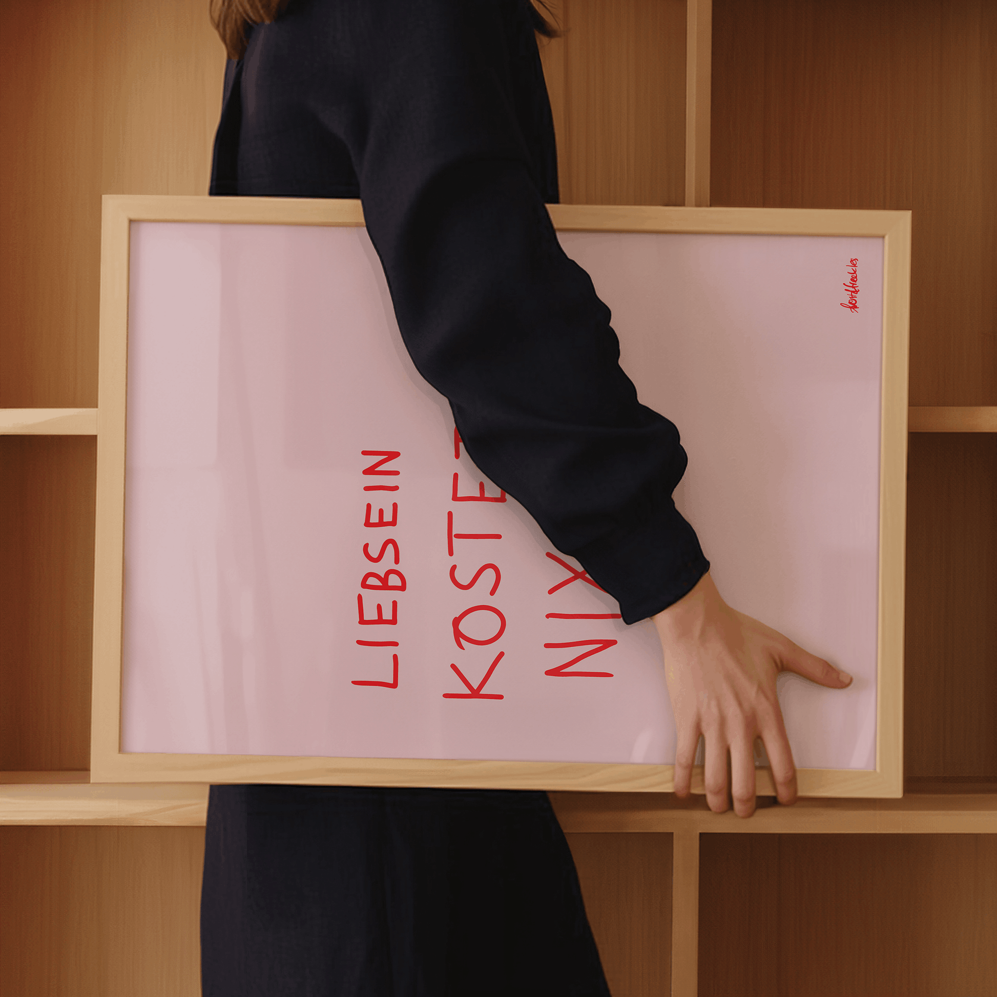 Frau trägt gerahmtes Küchenposter mit Schriftzug Liebsein Kostet Nix
