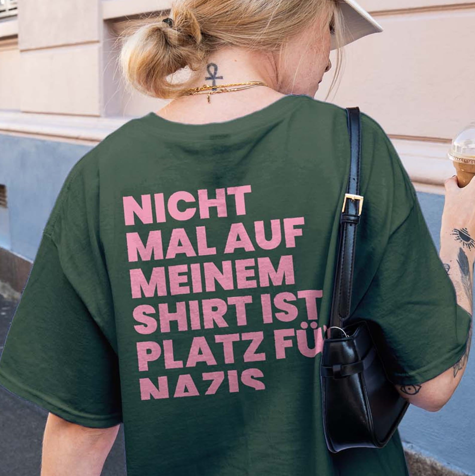 Rückansicht eines dunkelgrünen Oversized T-Shirts mit dem pinken Typografie-Aufdruck "Nicht mal auf meinem Shirt ist Platz für Nazis" als klares Anti-Nazi-Statement.