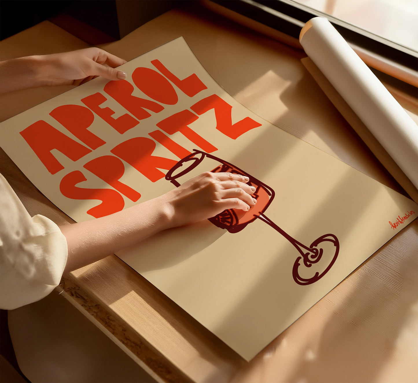 Aperol Spritz cocktail poster flat lay on beige background with woman's hands on top
