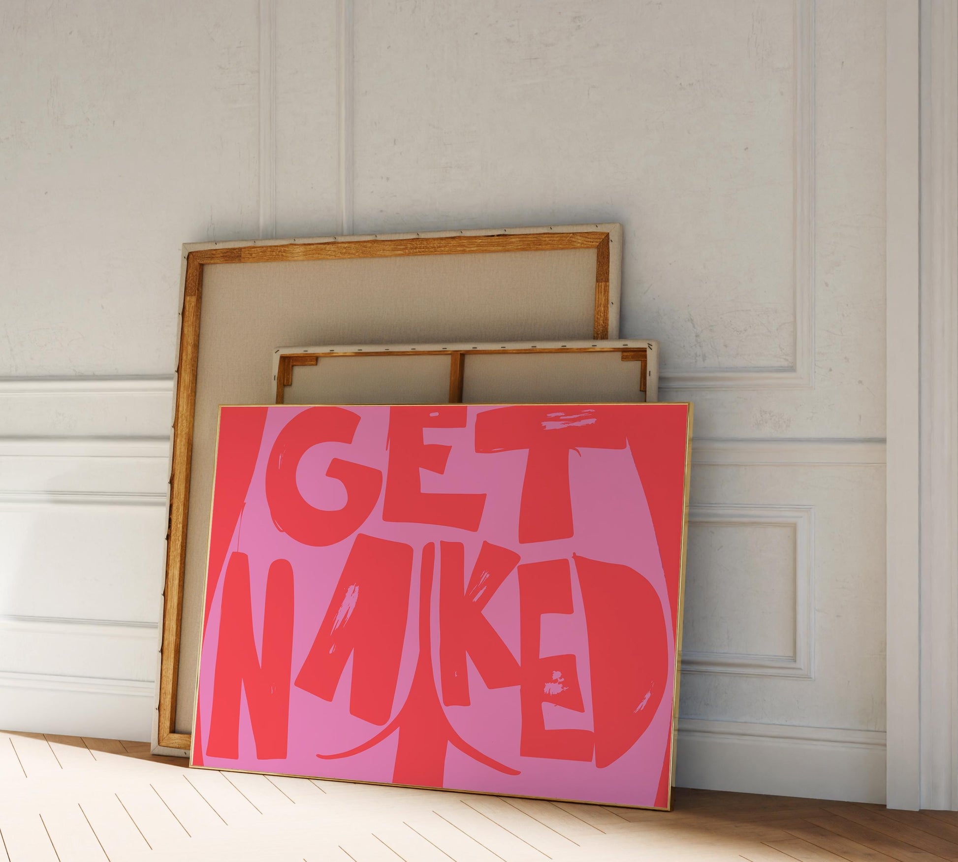 Colorful framed poster leaning against a wall, red and pink colors, showing a butt cheek illustration and the words "Get Naked".
