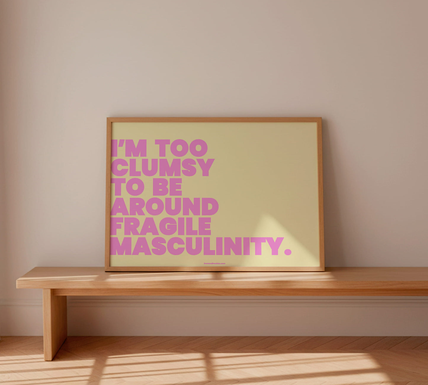 Ein farbenfrohes Statement-Wandbild "Fragile Masculinity" in Gelb und Pink, das in einem hellen Holzrahmen dekorativ an einer weißen Wand präsentiert wird.