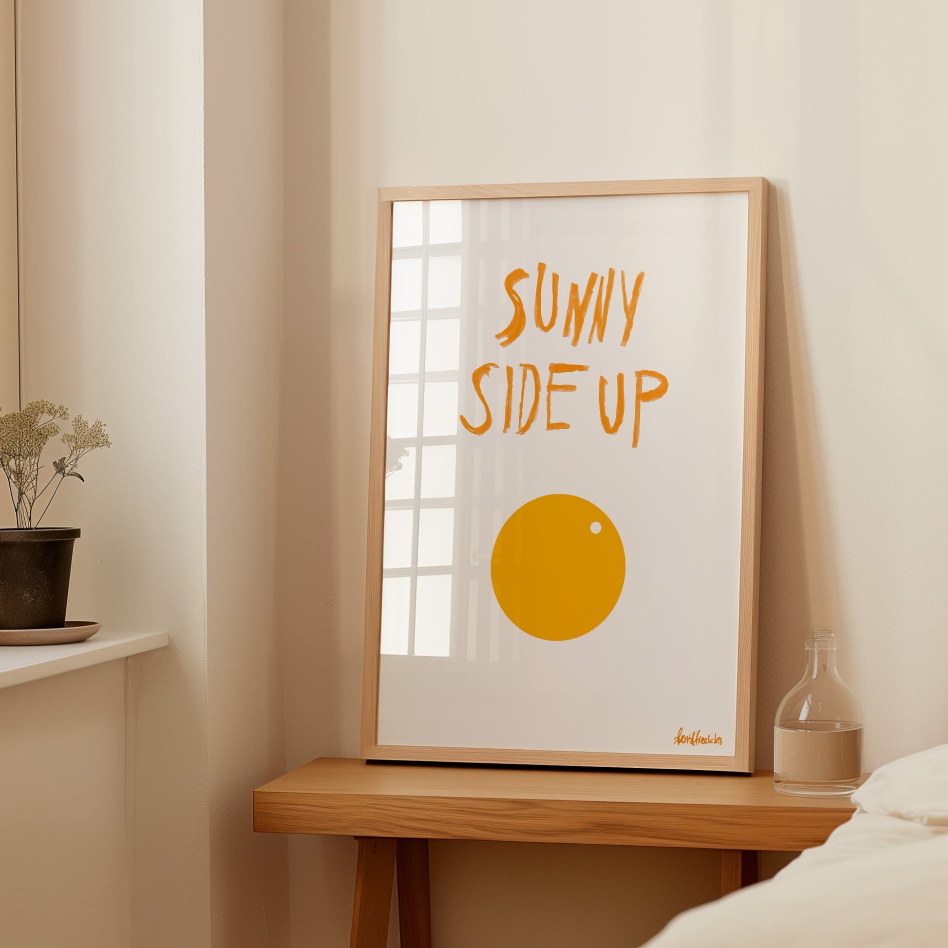 Framed Sunny Side Up Egg artwork styled with neutral warm accents on beside table