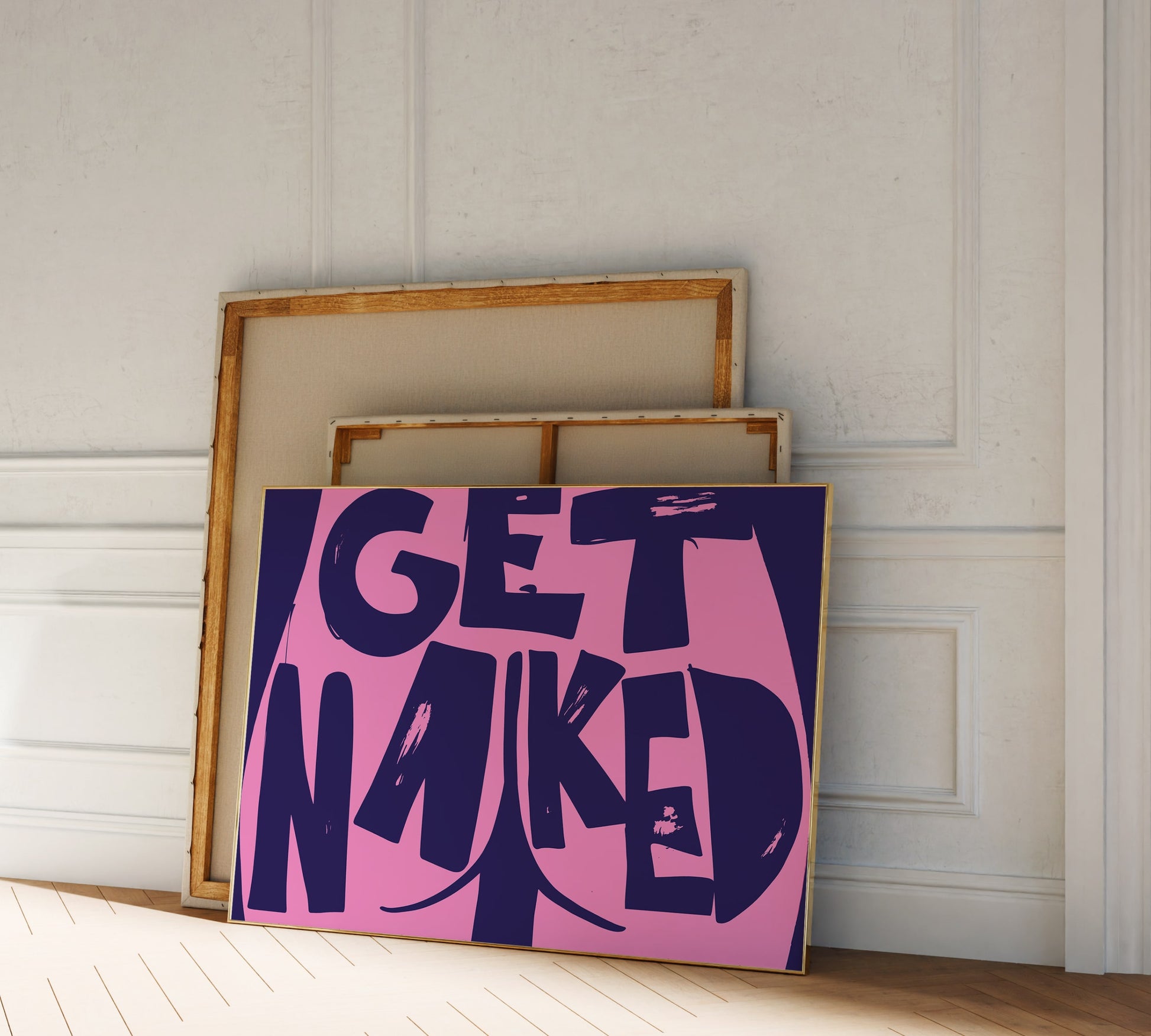 A picture frame leaning against a wall, bold purple pink lettering reading "Get Naked" with a butt cheek drawing at its center.
