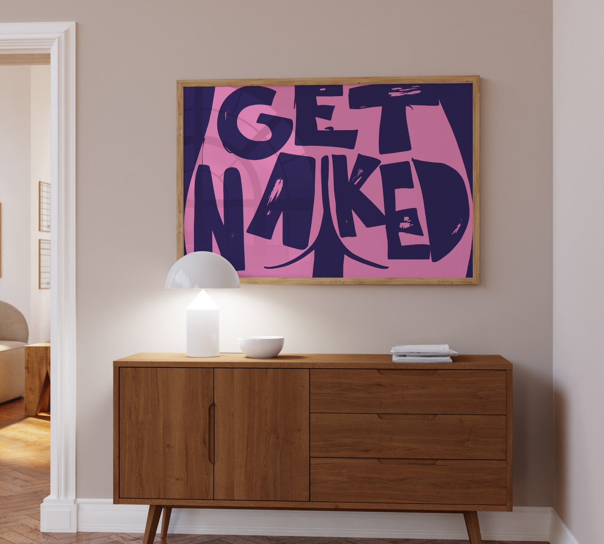 A bold bright pink and purple framed picture hanging above a bathroom sideboard, Danish minimalist design reading "Get Naked".
