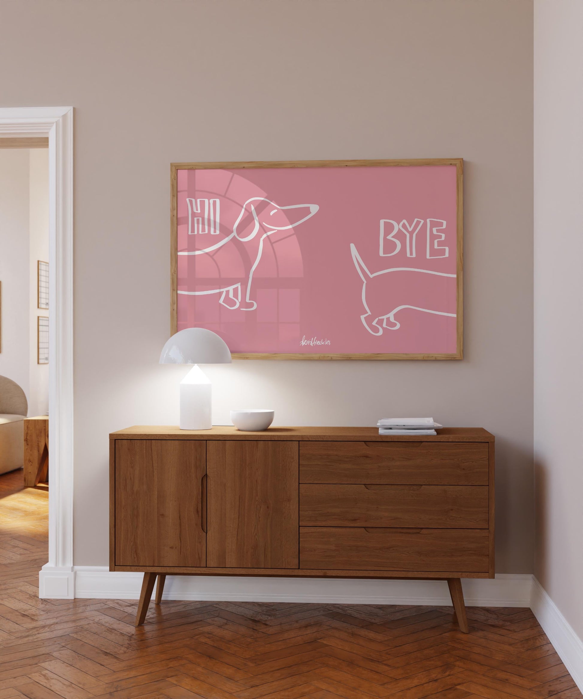 A bold pink picture hanging above a sideboard in entryway, Danish minimalist design showing a Dachshund illustration and the words "hi and bye".
