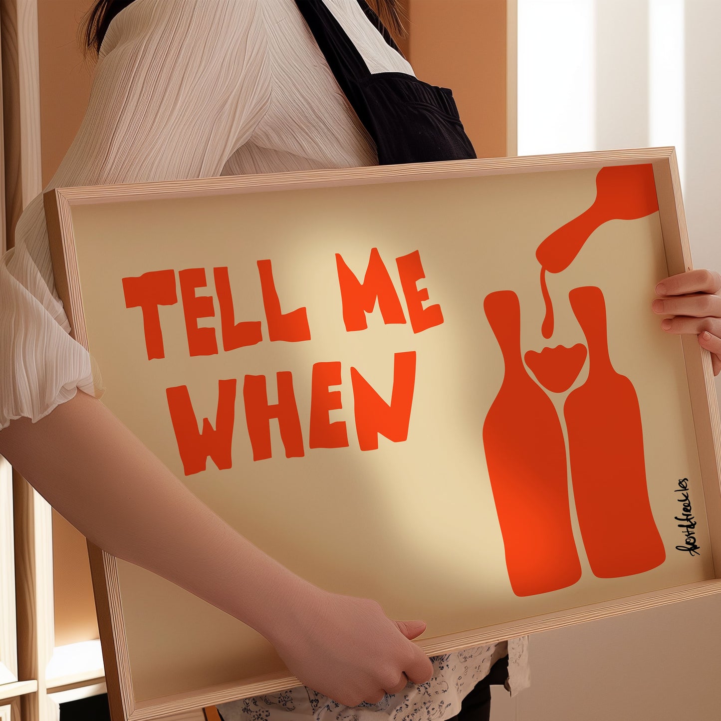Framed minimalist wine poster with 'Tell Me When' text held by waitress