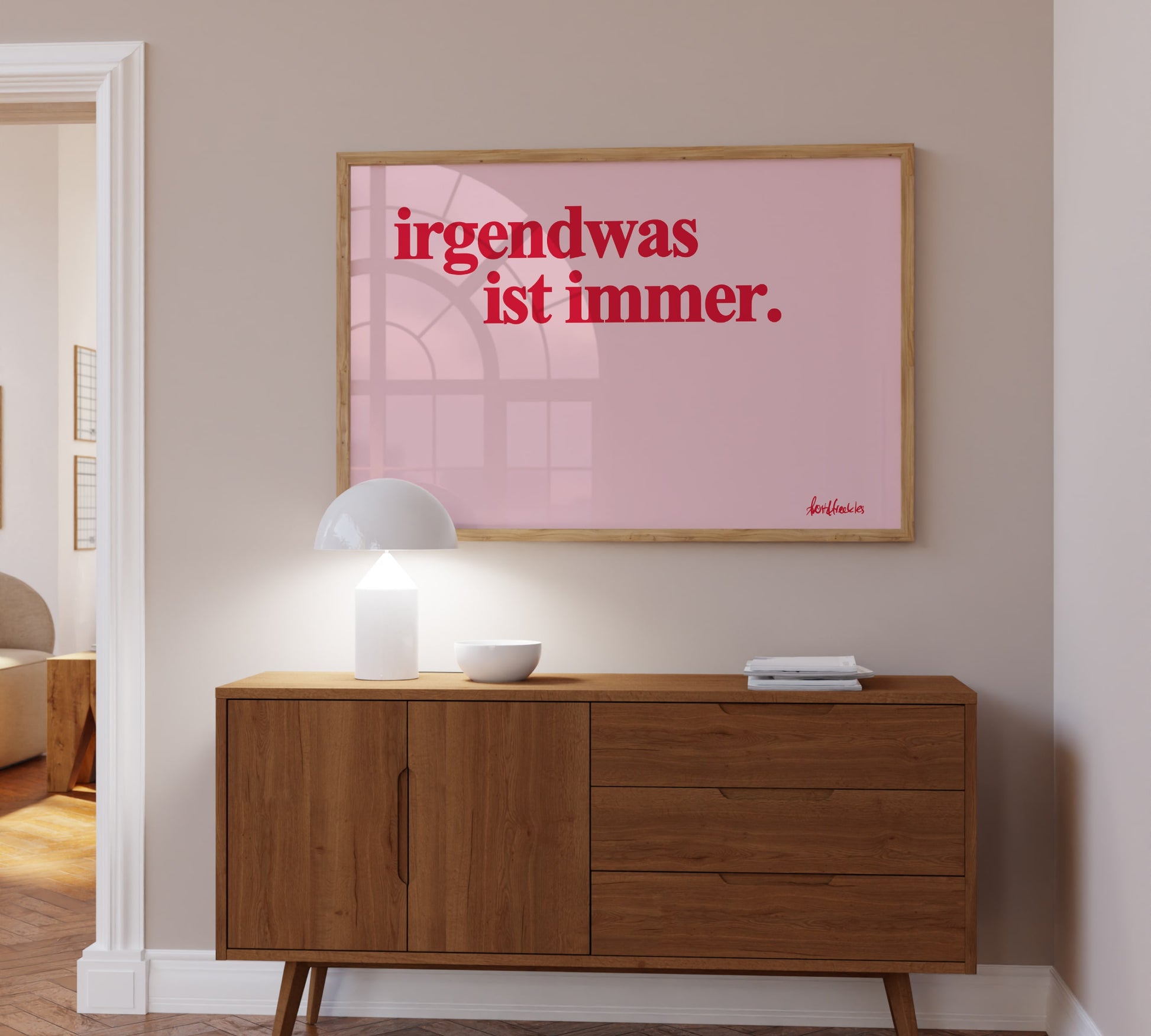 Gerahmtes Bild über Kommode mit "irgendwas ist immer" Zitat, roter Text auf pinkem Hintergrund.