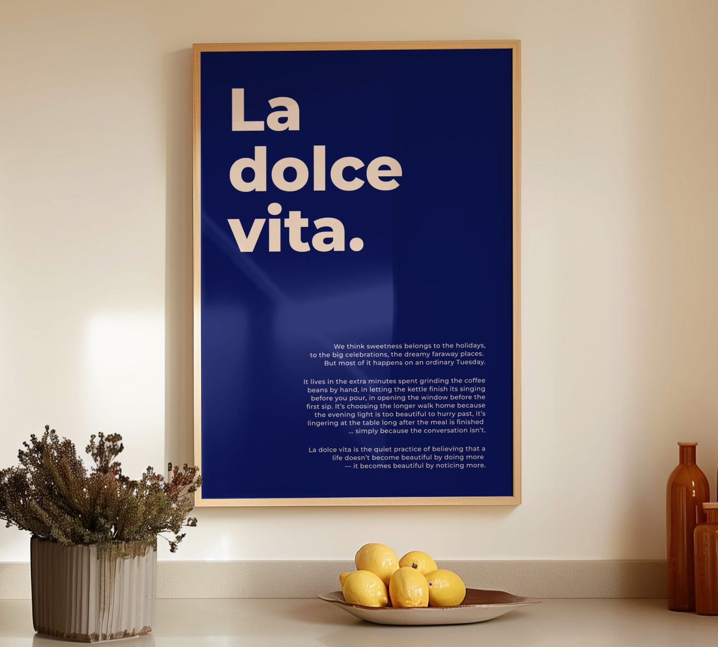 Framed Italy poster La dolce vita in a light wooden frame set on a kitchen counter next to fresh lemons and ceramic vases.