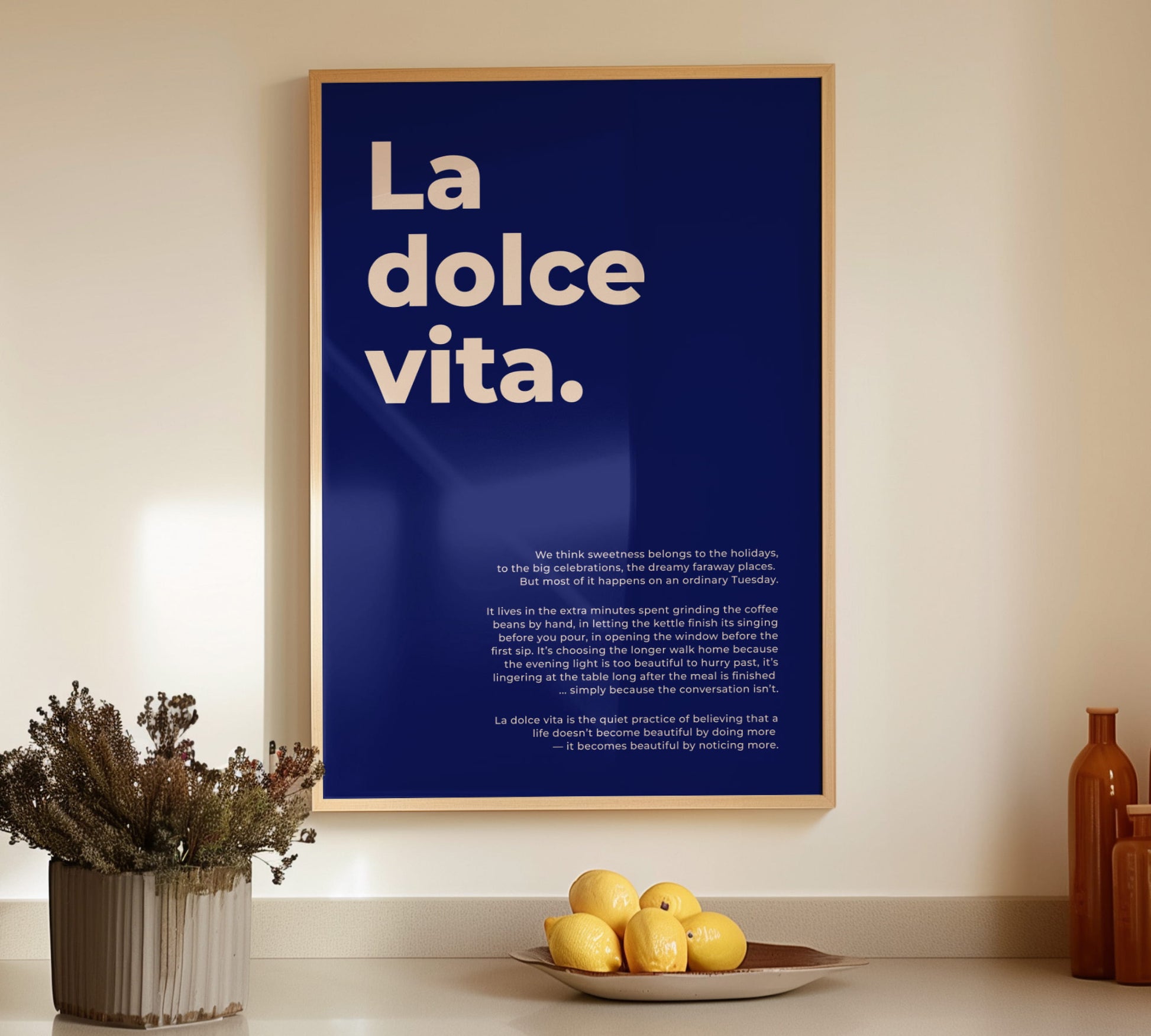 Framed Italy poster La dolce vita in a light wooden frame set on a kitchen counter next to fresh lemons and ceramic vases.