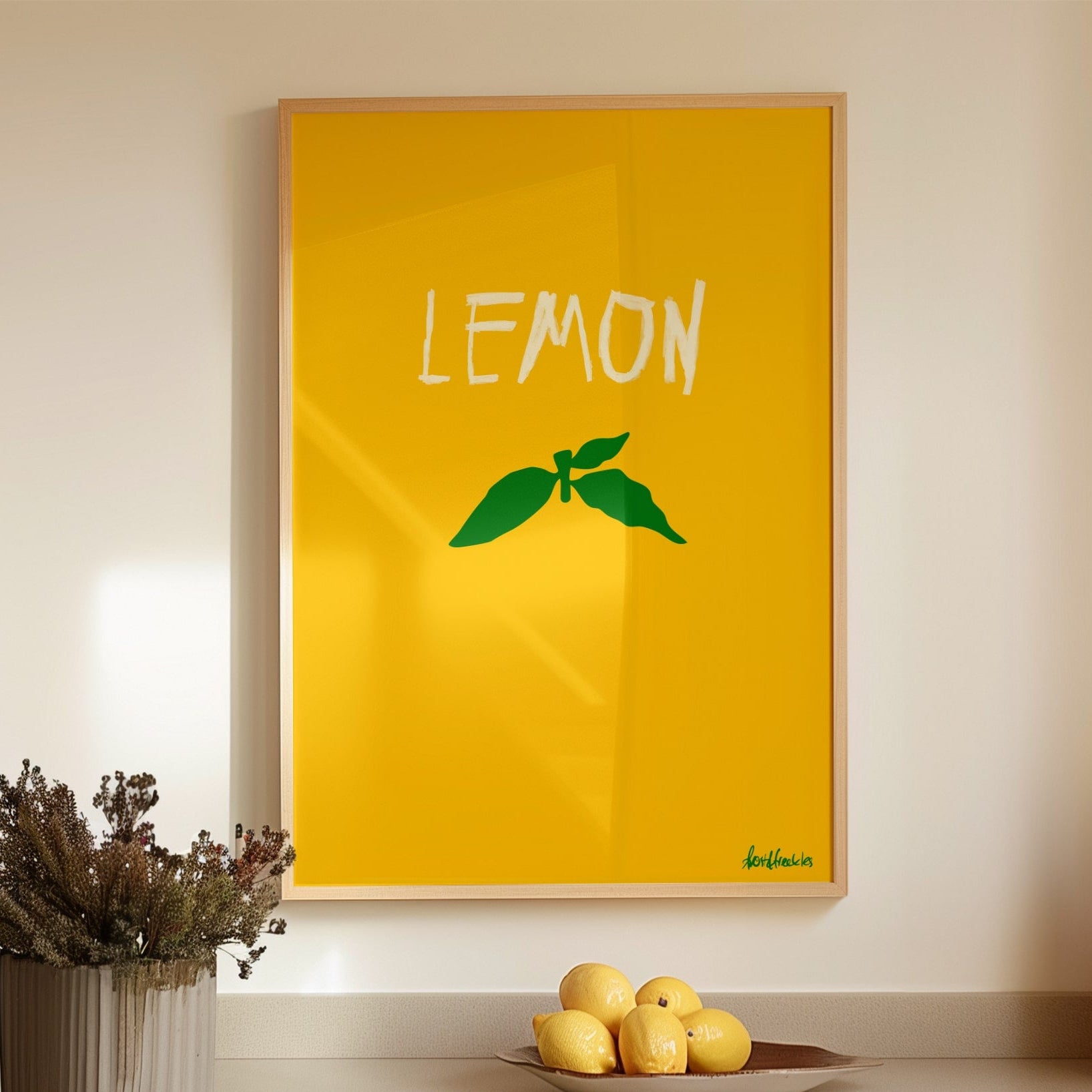 Minimalist lemon poster print with green stem design in a modern kitchen setting with lemons on counter.