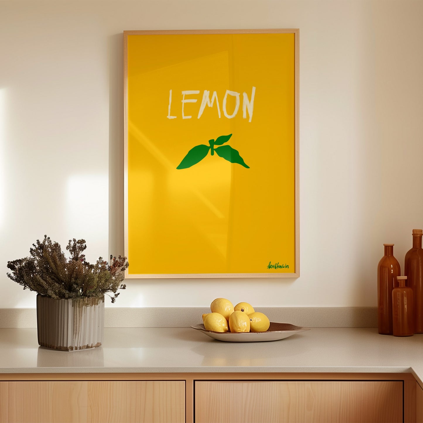 Minimalist lemon poster print with green stem design in a modern kitchen setting with lemons on counter.