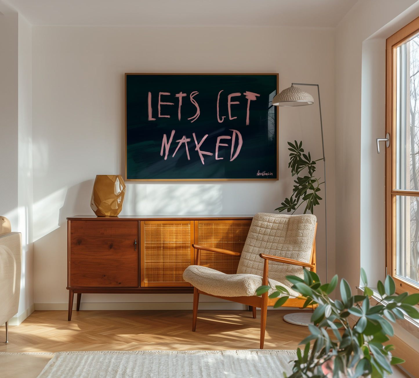 Modern framed oil brush lettering reading "Let's Get Naked" in a neutral-toned bedroom with natural light