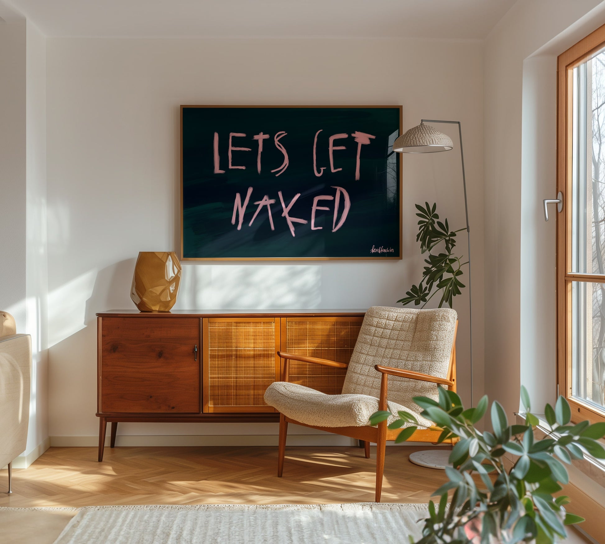 Modern framed oil brush lettering reading "Let's Get Naked" in a neutral-toned bedroom with natural light