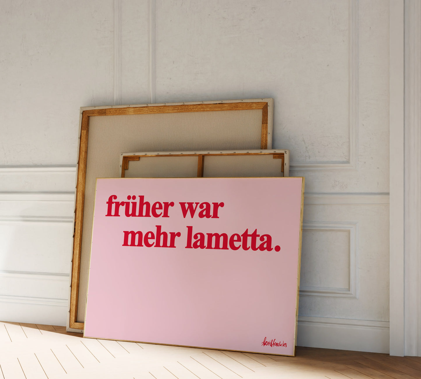 Two canvases lean against a white wall; the front canvas is pink with red German text reading "Früher war mehr Lametta" - a quote by Loriot.