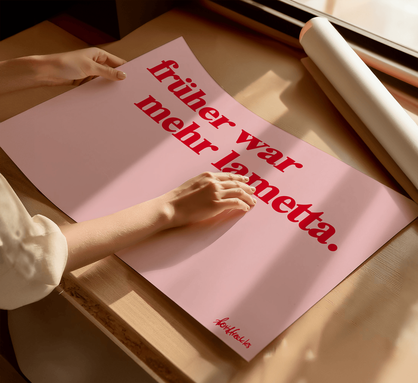 A woman holding a pink poster with the German phrase “Früher war mehr Lametta", a quote by Loriot, in bold red text, on a wooden table near a window with sunlight.