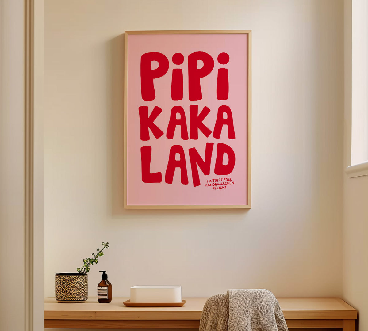 Gerahmtes Klo-Wandbild „Pipi Kaka Land“ in einem hellen Holzrahmen an der Wand in modernem Badezimmer.