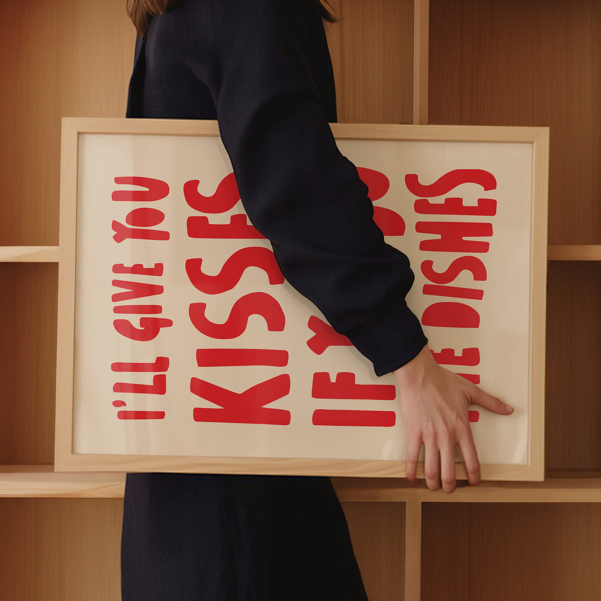 Frau trägt gerahmtes Küchen-Poster „Kisses if you do the dishes“ in einem Holzrahmen unter dem Arm in moderner Scandi Küche