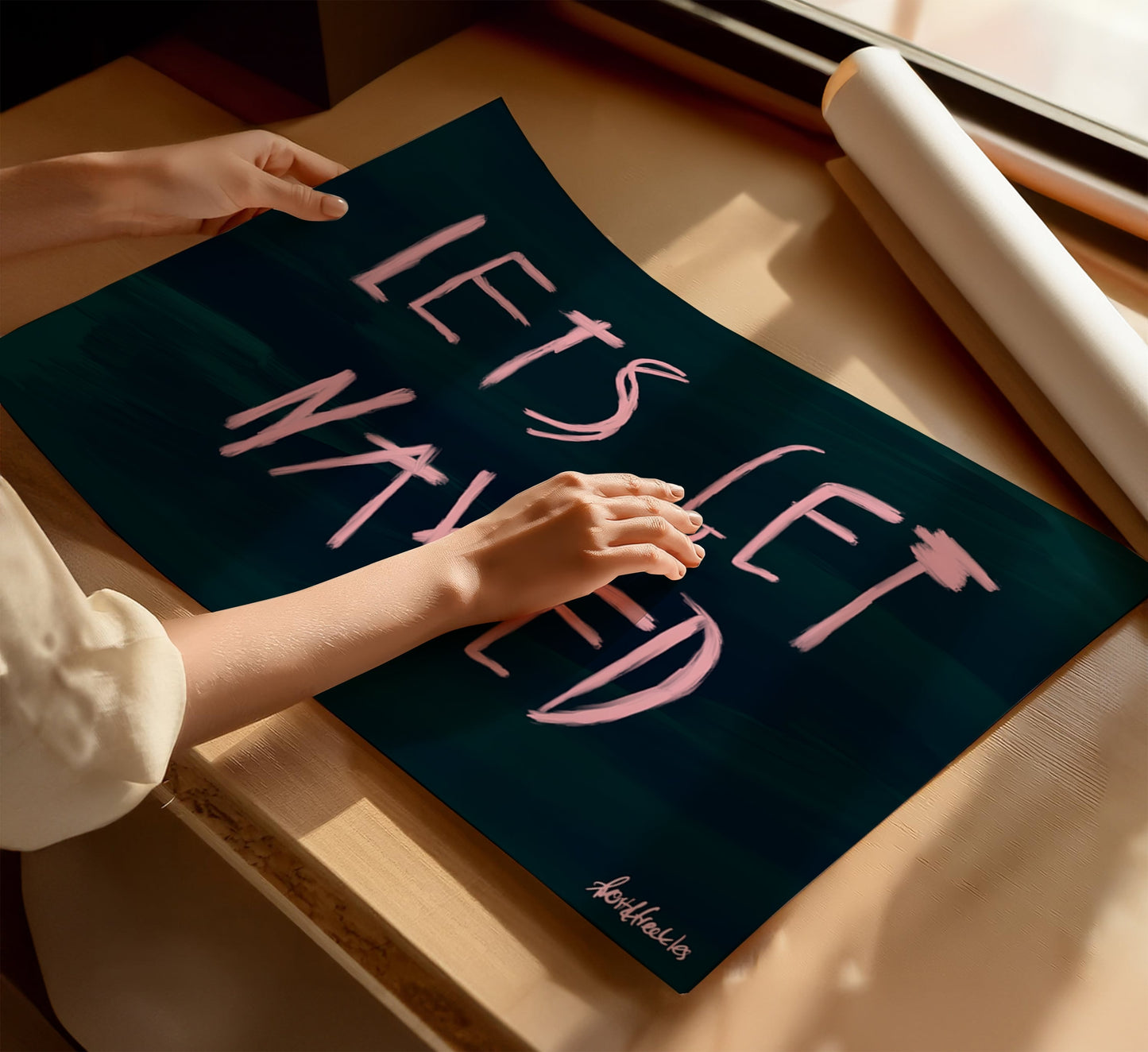Closeup of oil-brush style "Let’s Get Naked" poster rolled out flat on a wooden table