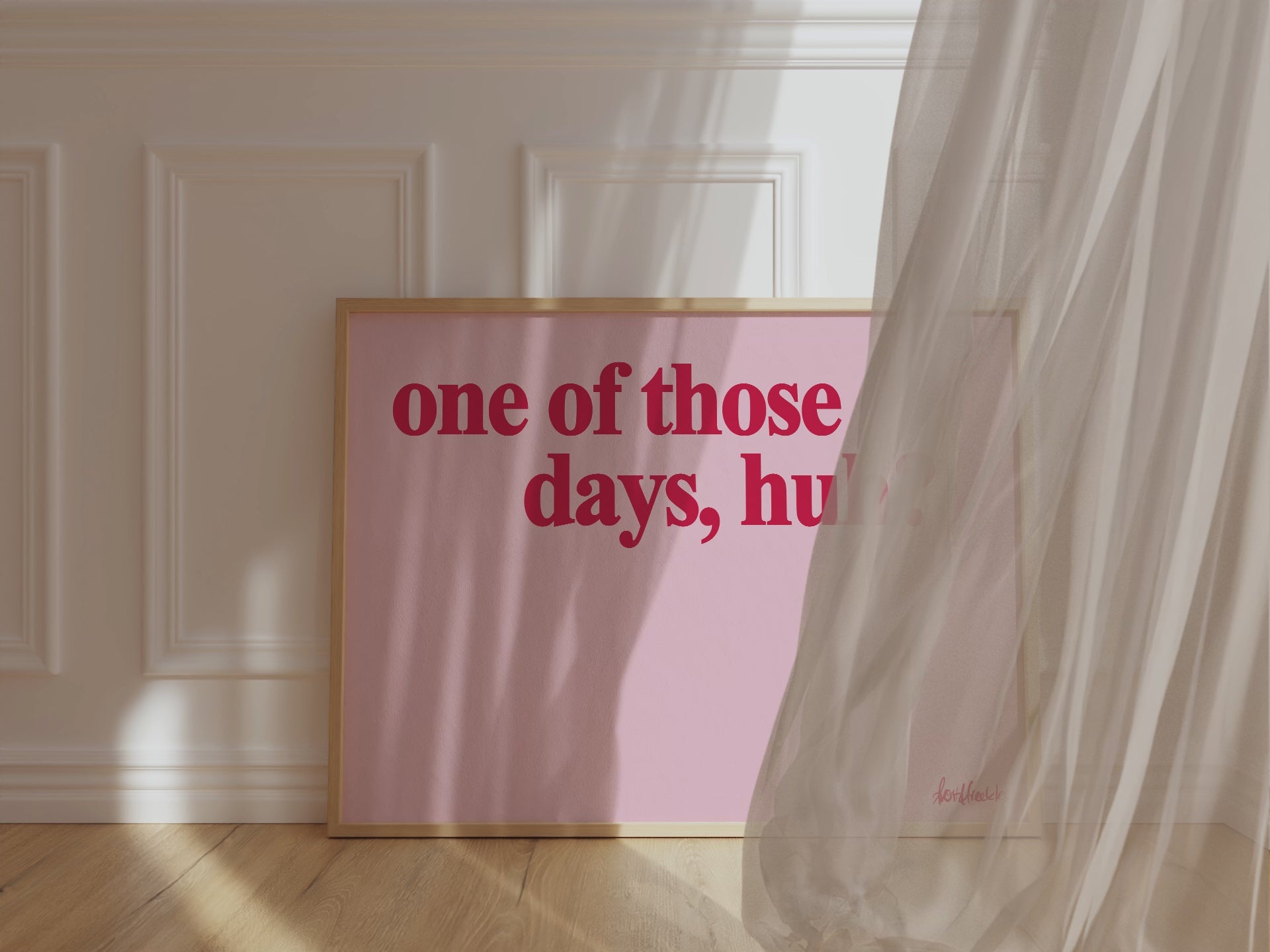 A framed picture leaning against a bedroom wall, pink background and bold red letters reading "one of those days huh", wind blowing the curtain around.