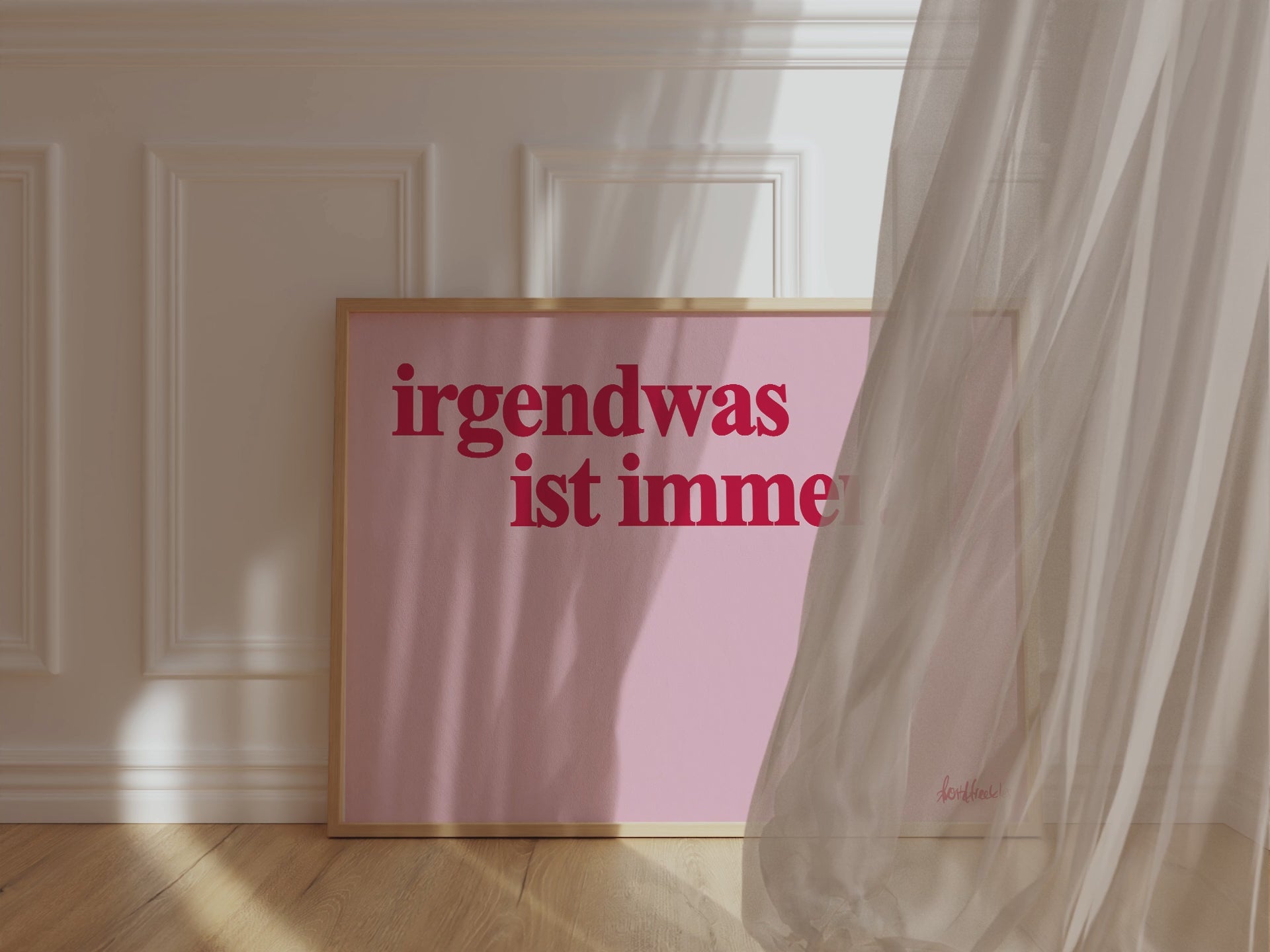 Ein gerahmtes, horizontales Poster zeigt den Spruch "Irgendwas ist immer" in roter Schrift auf pinkem Hintergrund. Der Wind weht einen Vorhang vor den Rahmen und verdeckt diesen teilweise. 