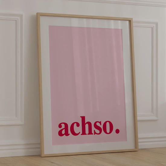 Gerahmtes "Achso" Poster in modernen Farben lehnt an einer Wand.