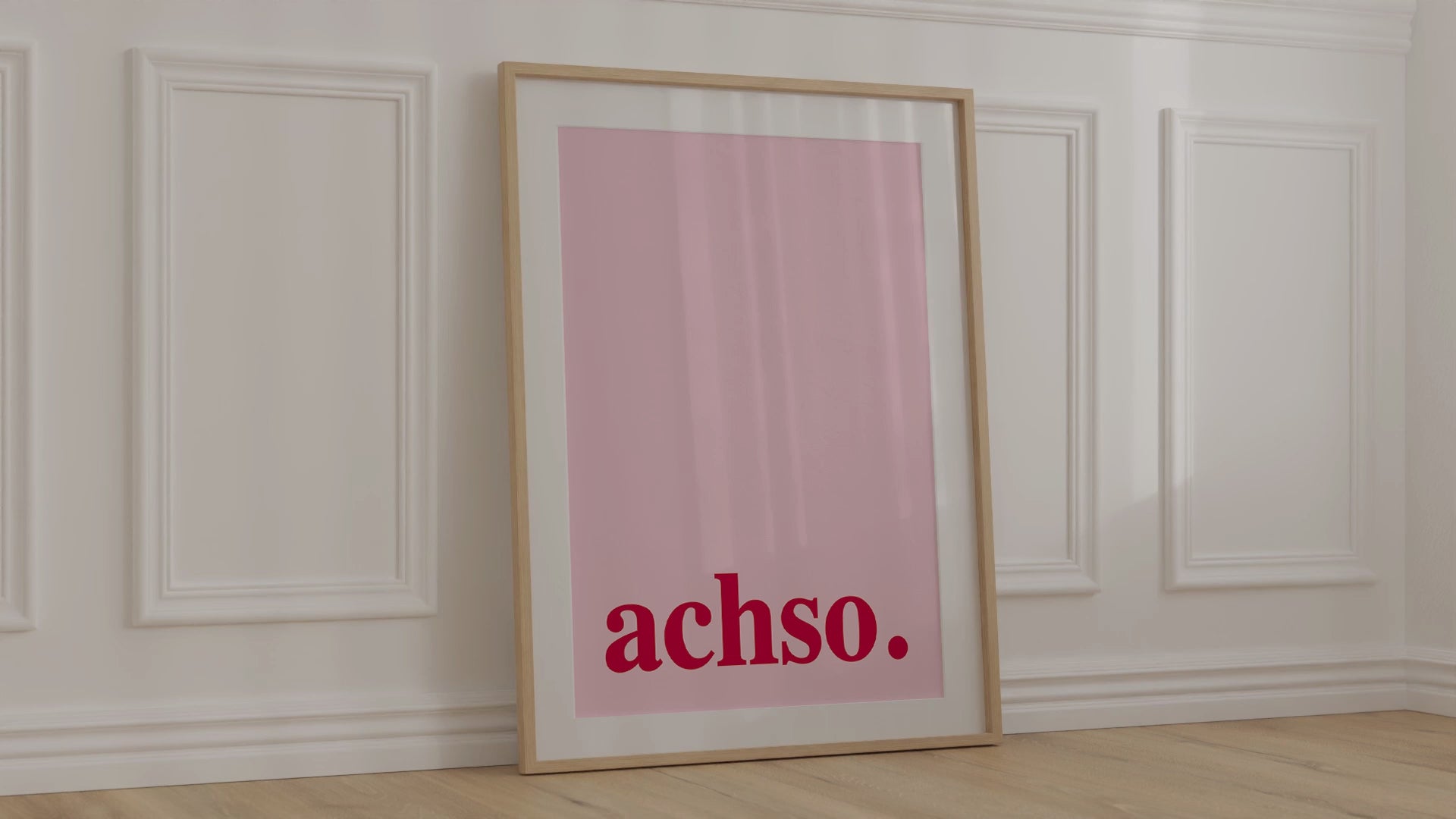 Gerahmtes "Achso" Poster in modernen Farben lehnt an einer Wand.