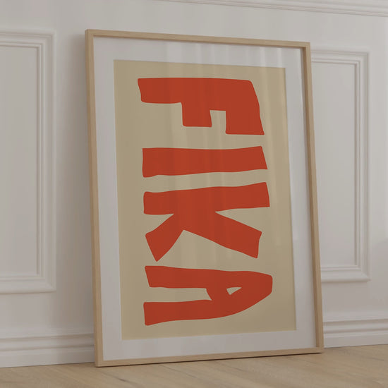 A modern, minimalist print of the Swedish word "FIKA" for coffee break in big bold orange letters on a warm beige background.