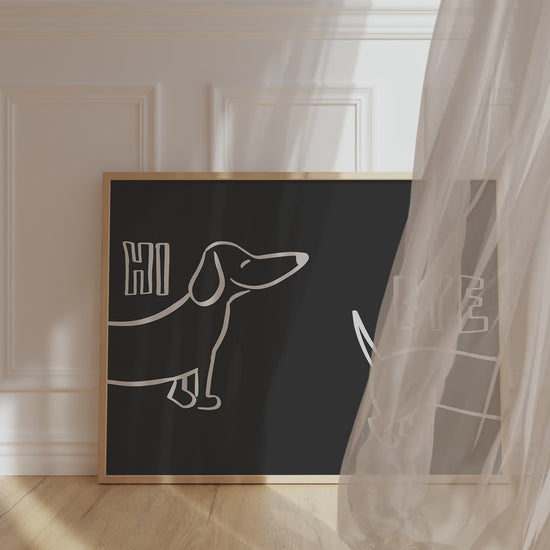 A framed picture leaning against a hallway wall, black background and bold white letters reading "Hi Bye", with cute sausage dog illustration in center.