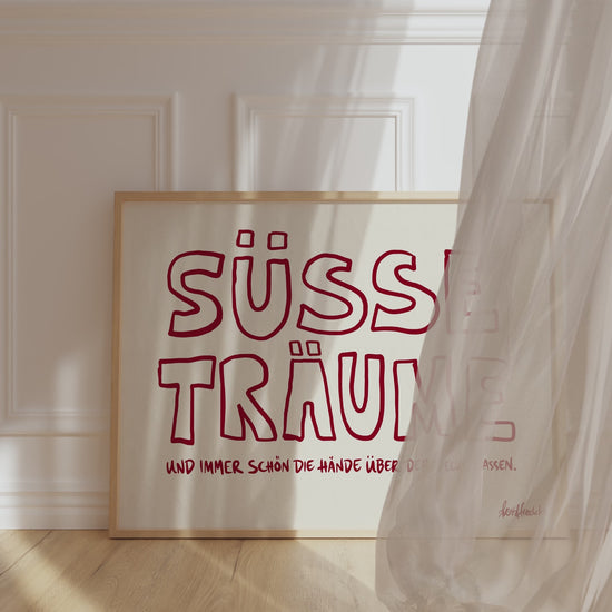 Ein Bilderrahmen lehnt gegen eine Schlafzimmer Wand, im horizontalen Format ist der Text "Süße Träume" in moderner Typografie zu lesen.