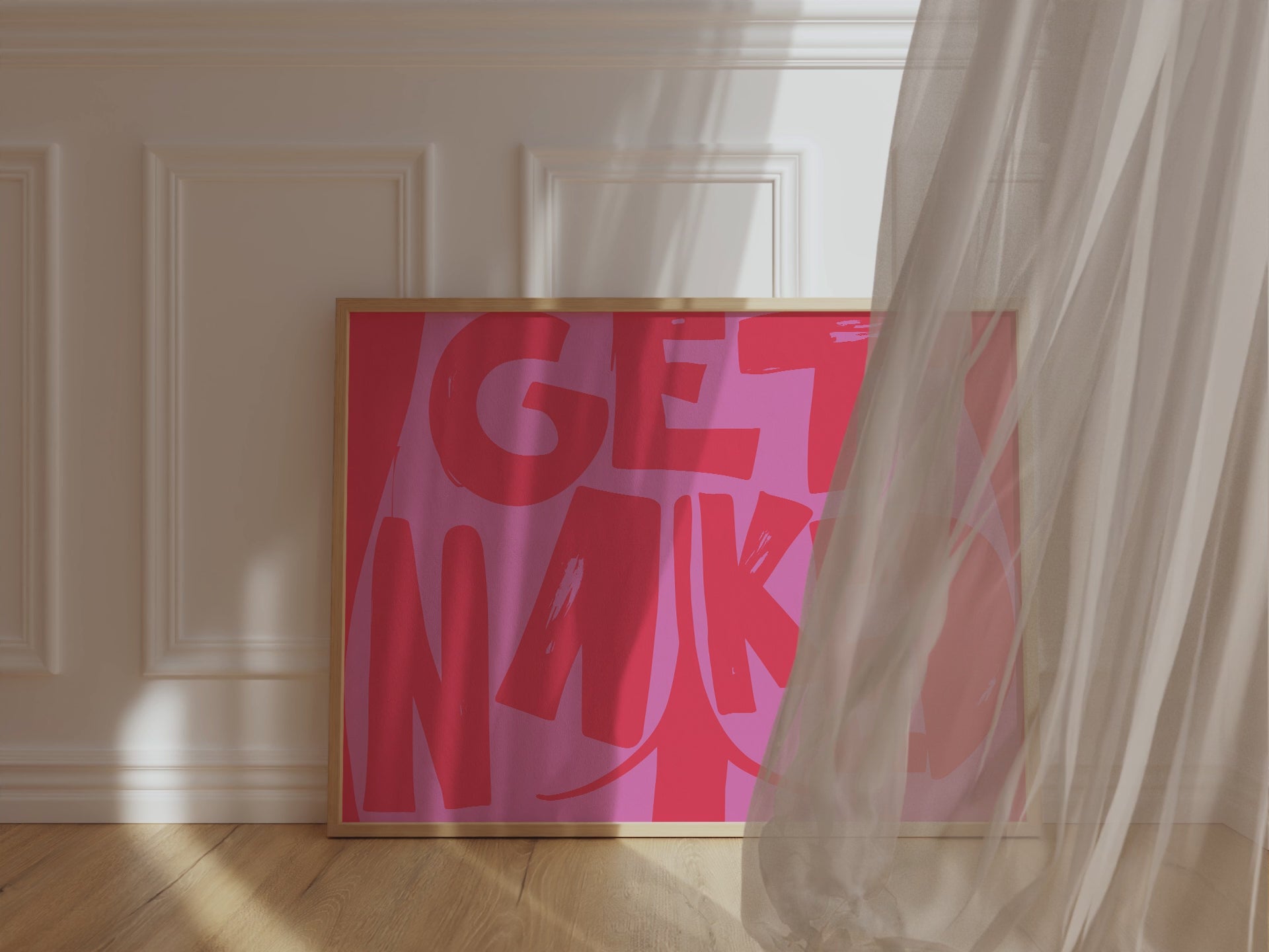 A framed picture leaning against a bathroom wall, red background and bold pink letters reading "Get Naked" with a butt cheek drawing in its center.