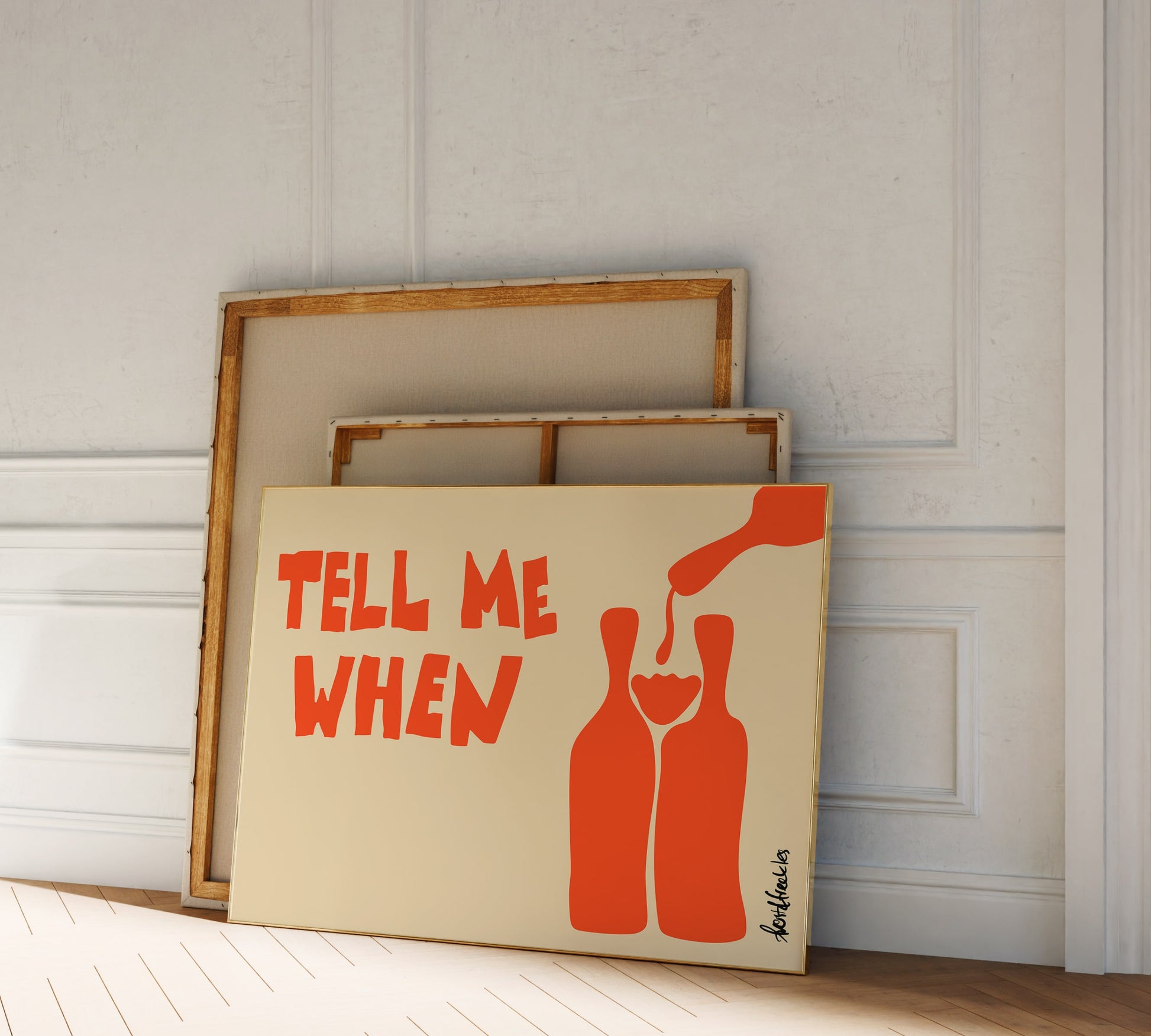 Framed wine poster reading "Tell Me When" as part of a gallery wall with neutral decor in hallway